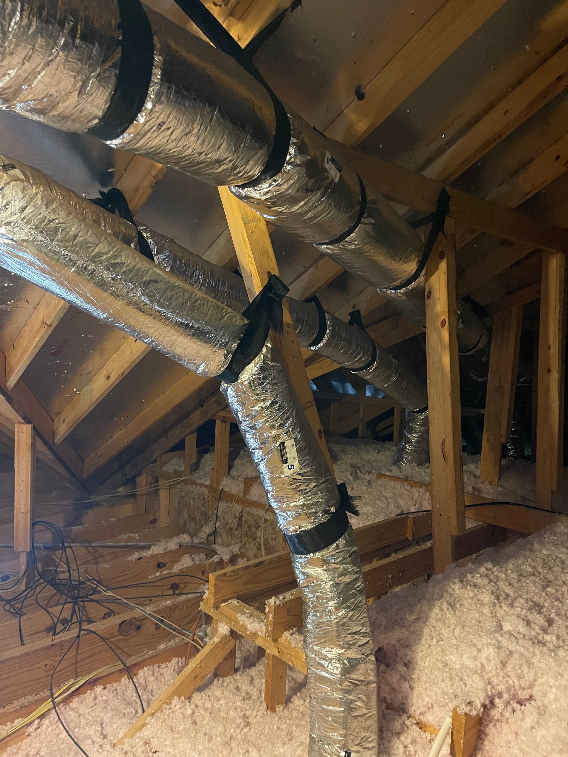 Foil-wrapped HVAC ducts and flexible vent hoses in an unfinished attic with exposed rafters