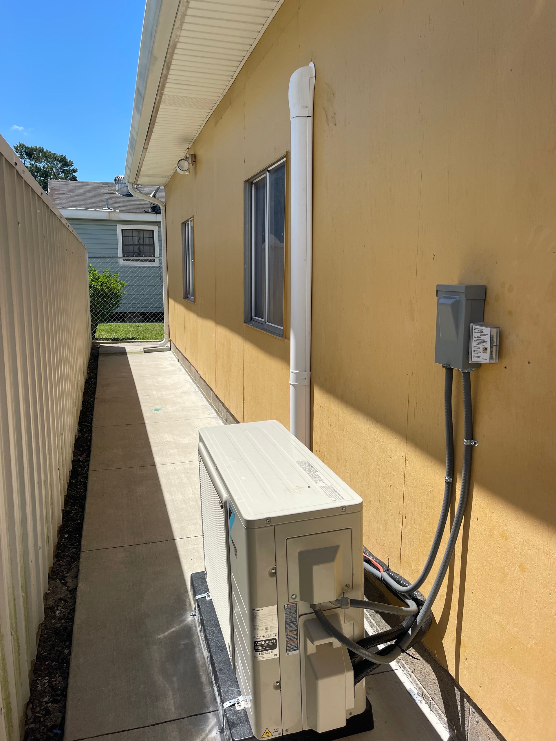 Narrow outdoor side yard with a beige building, utility equipment, and electrical boxes along the wall.