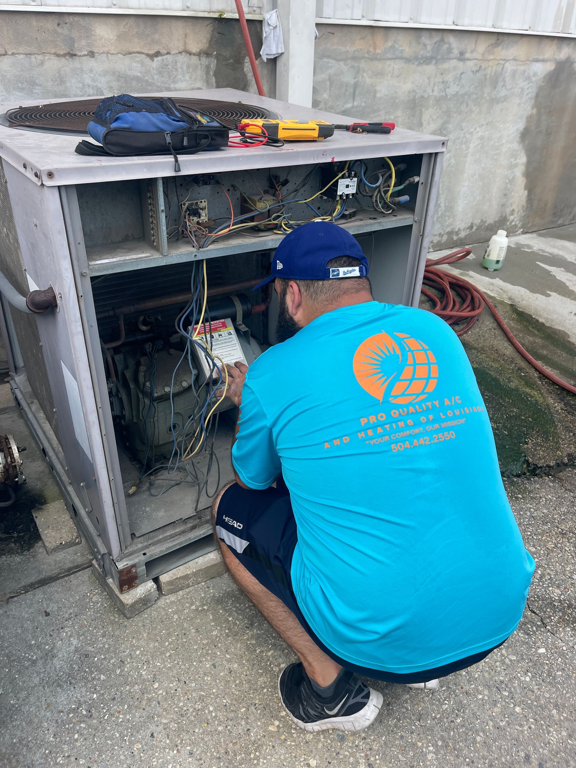Technician in blue shirt inspecting an open HVAC unit outdoors