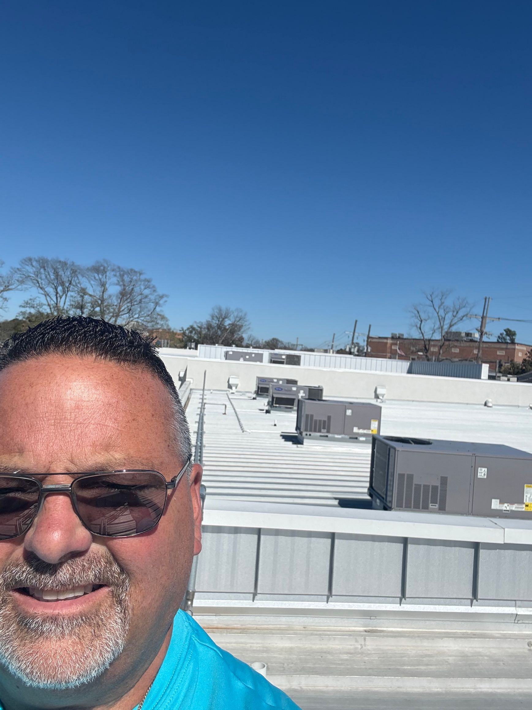 Person taking a selfie on a bright rooftop with white vents and a clear blue sky