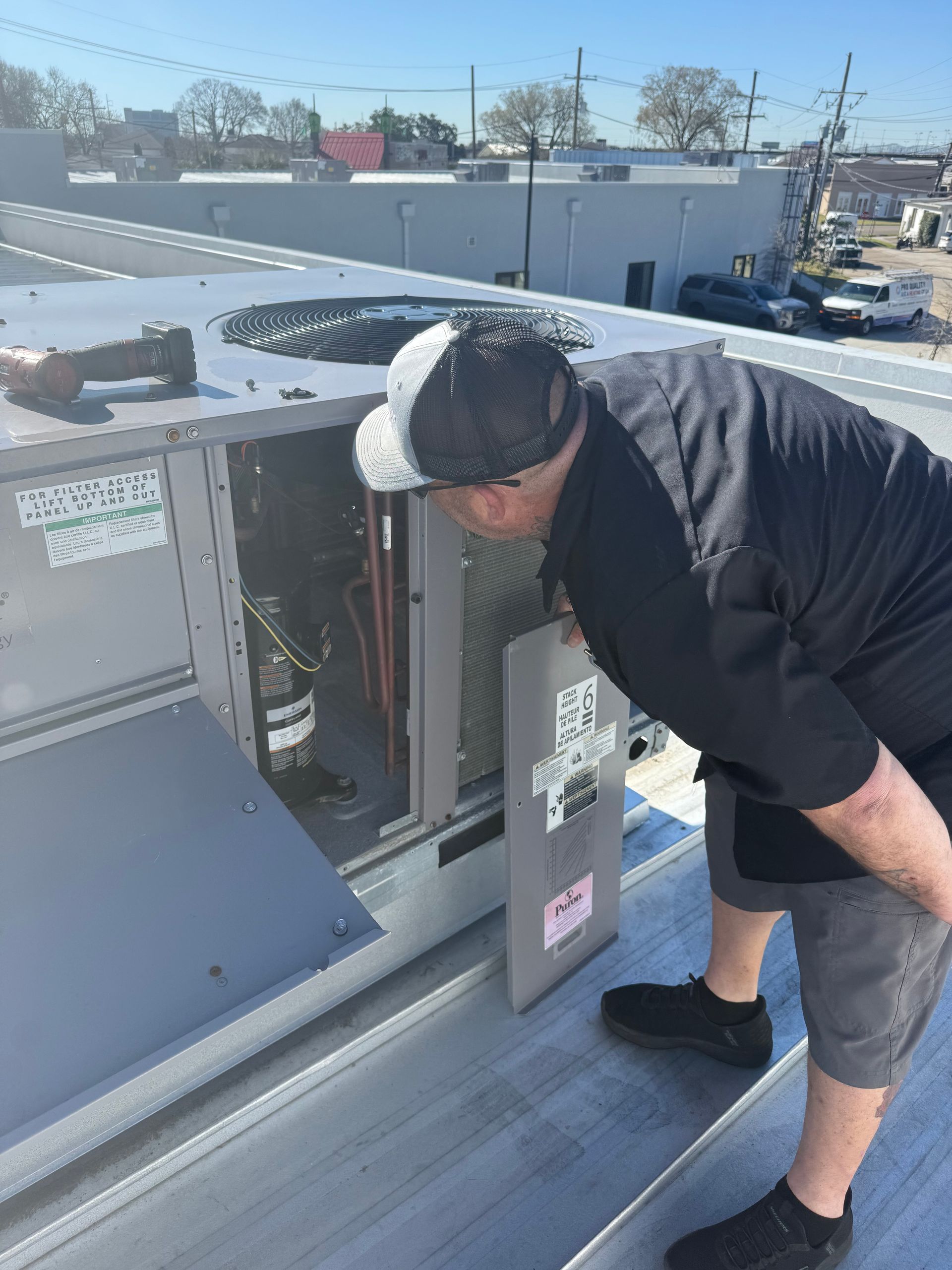 Worker leaning into rooftop HVAC unit for inspection on a sunny day