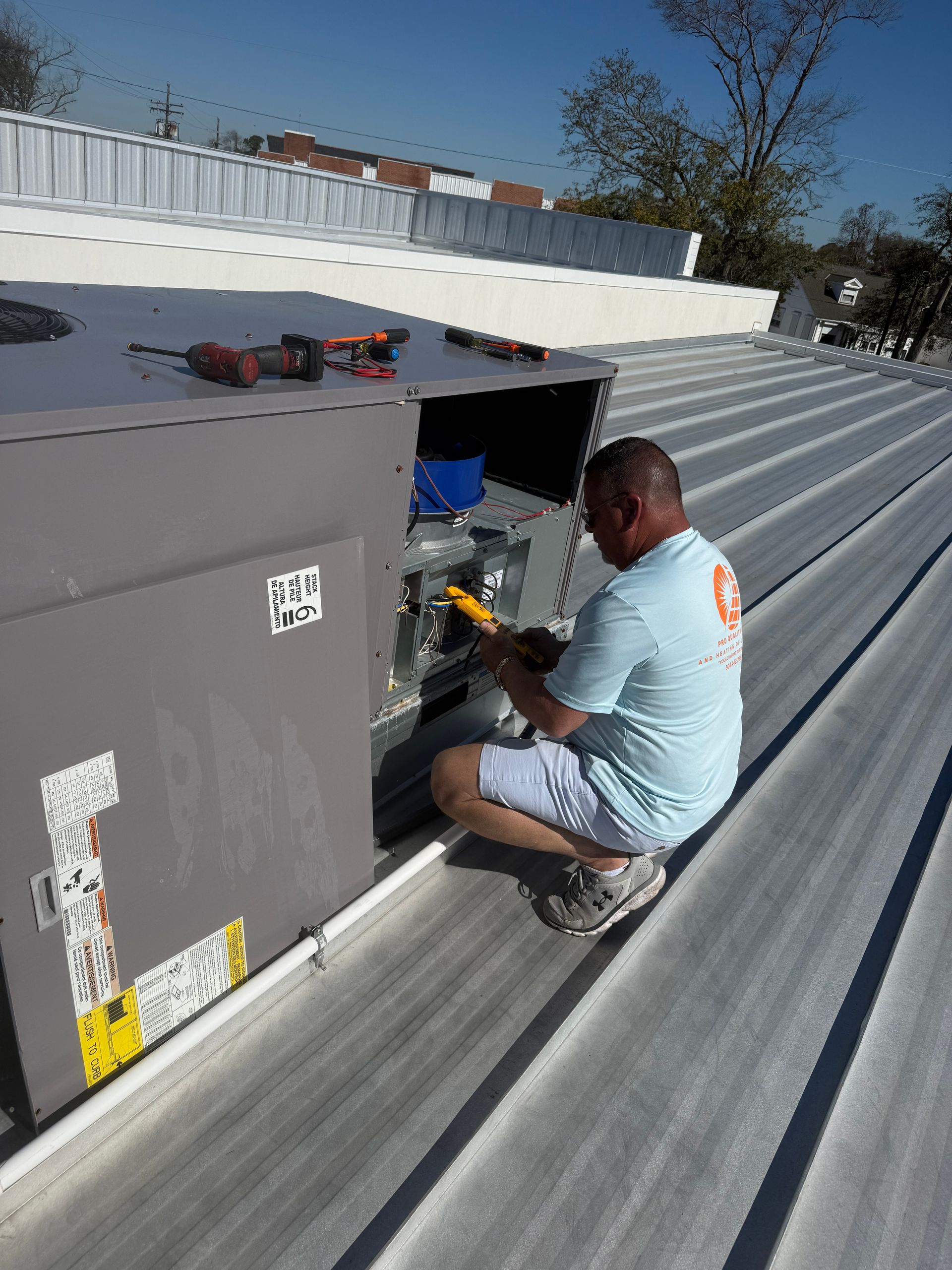 Technician repairing rooftop HVAC unit on a corrugated metal roof under clear skies