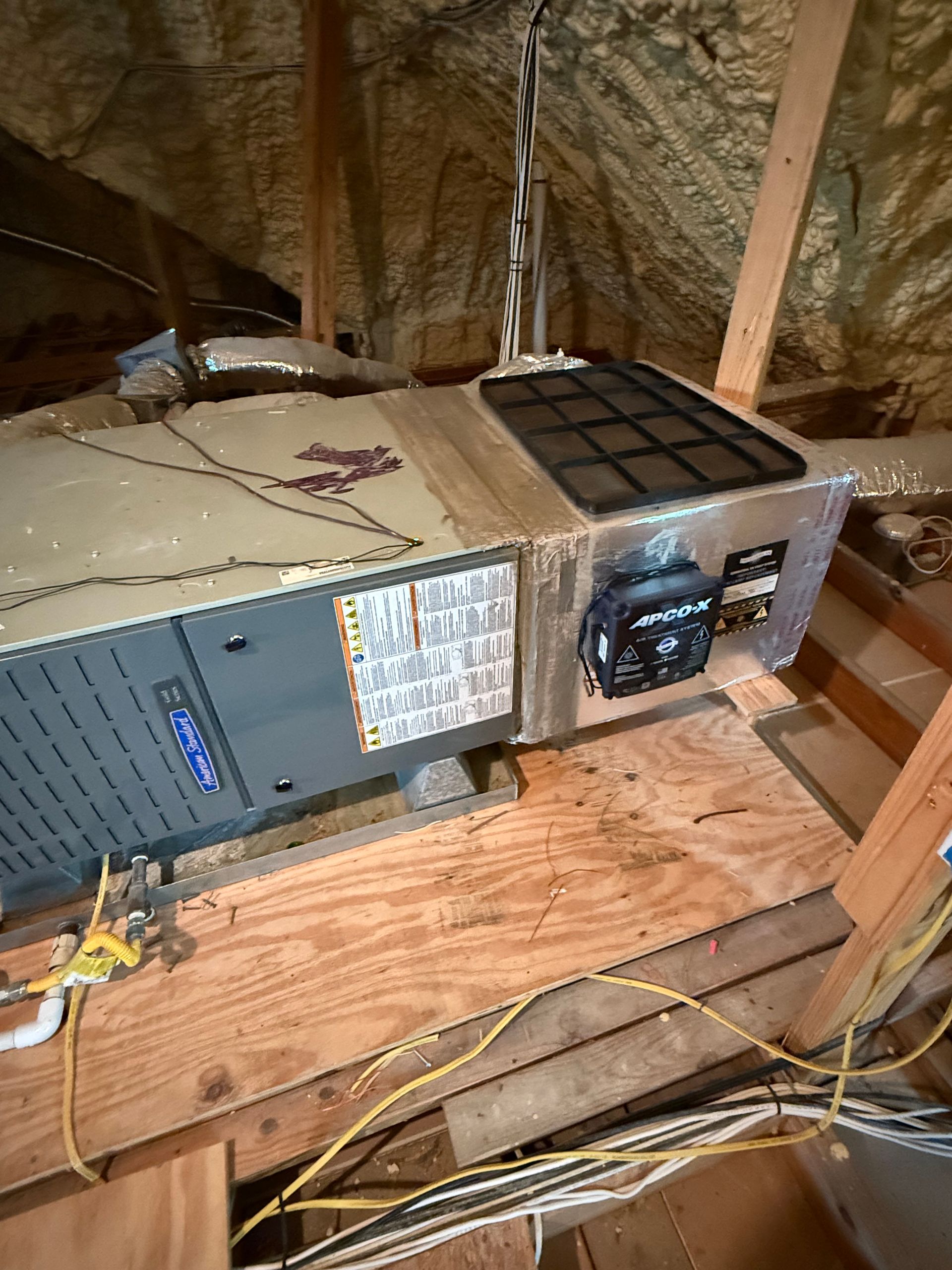 Old HVAC unit in a dusty attic with exposed wooden beams and loose wires.
