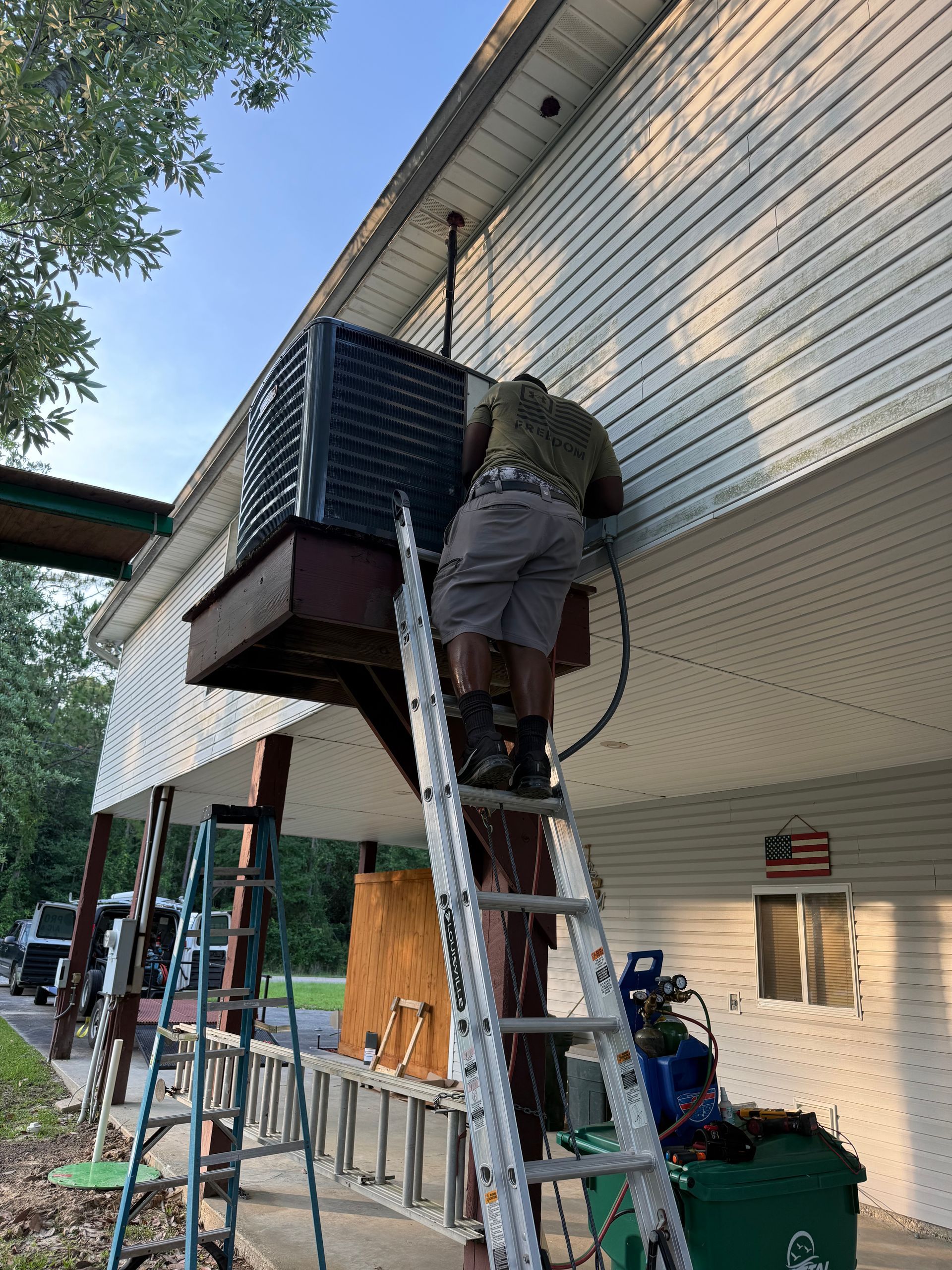 Person on ladder working on the side of a house with a balcony and scaffolding below