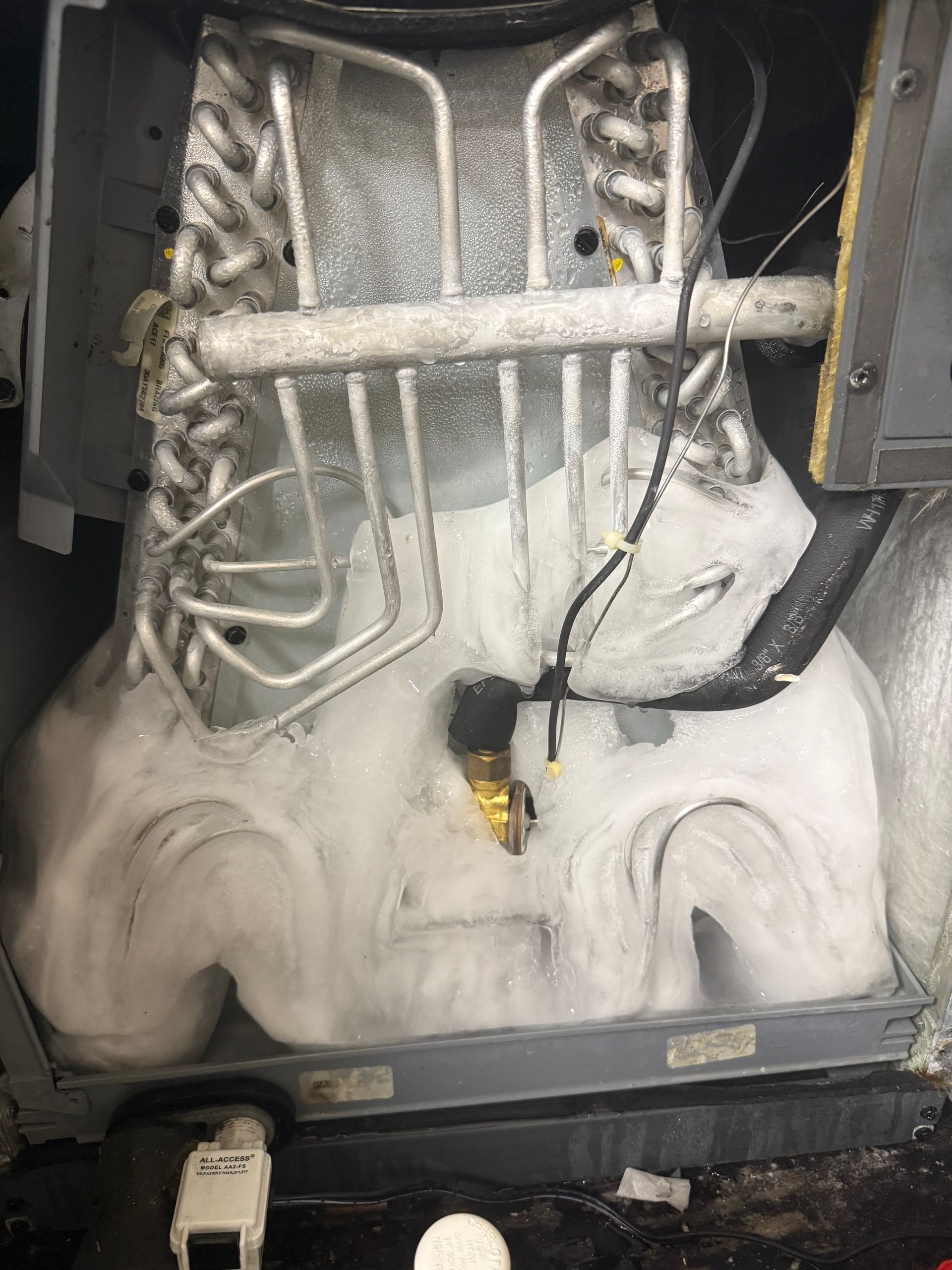 Snow-covered machinery with hoses and metal tubing inside an open compartment