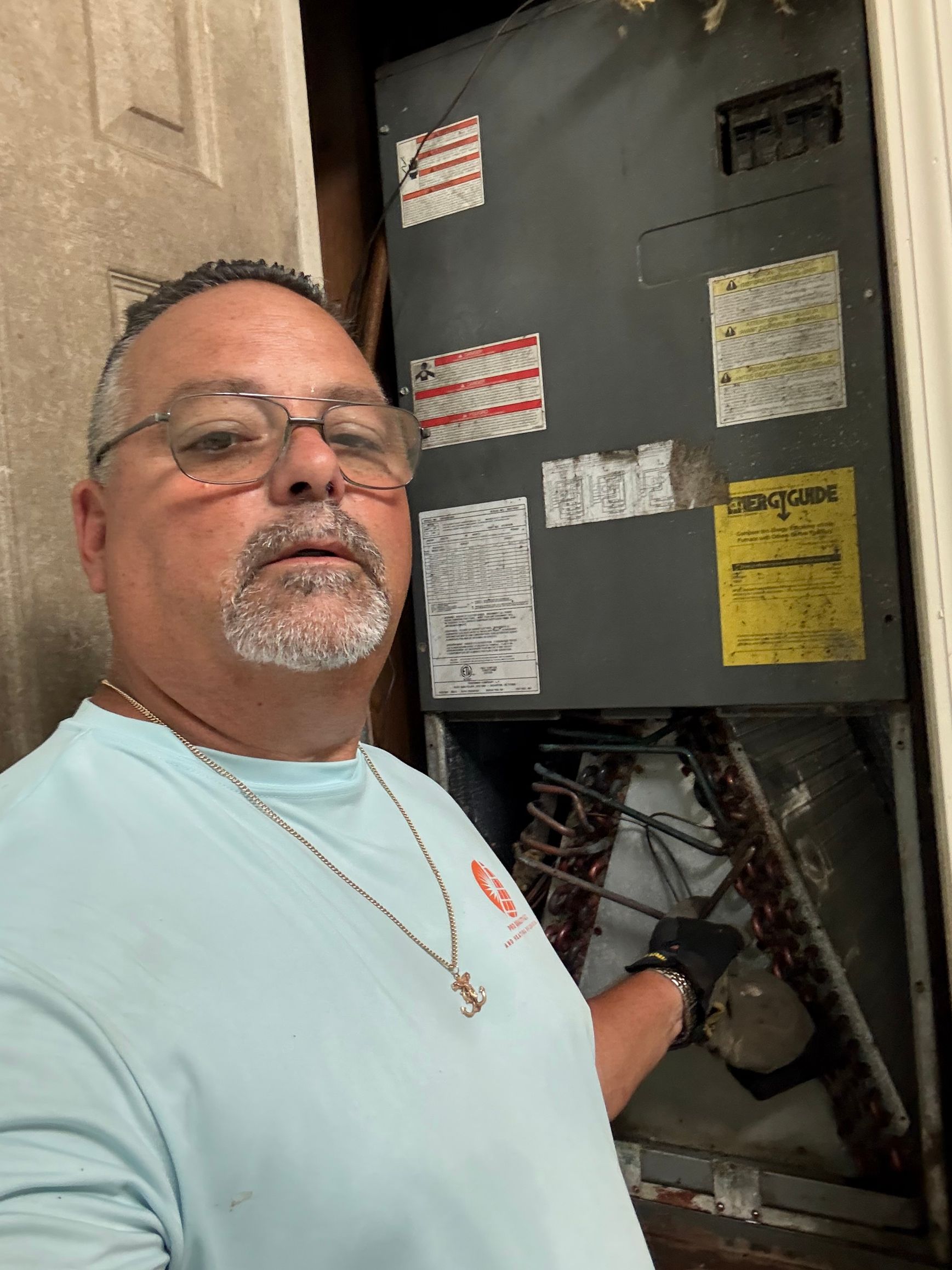 Man standing beside an open electrical panel, holding exposed wiring in a utility area.