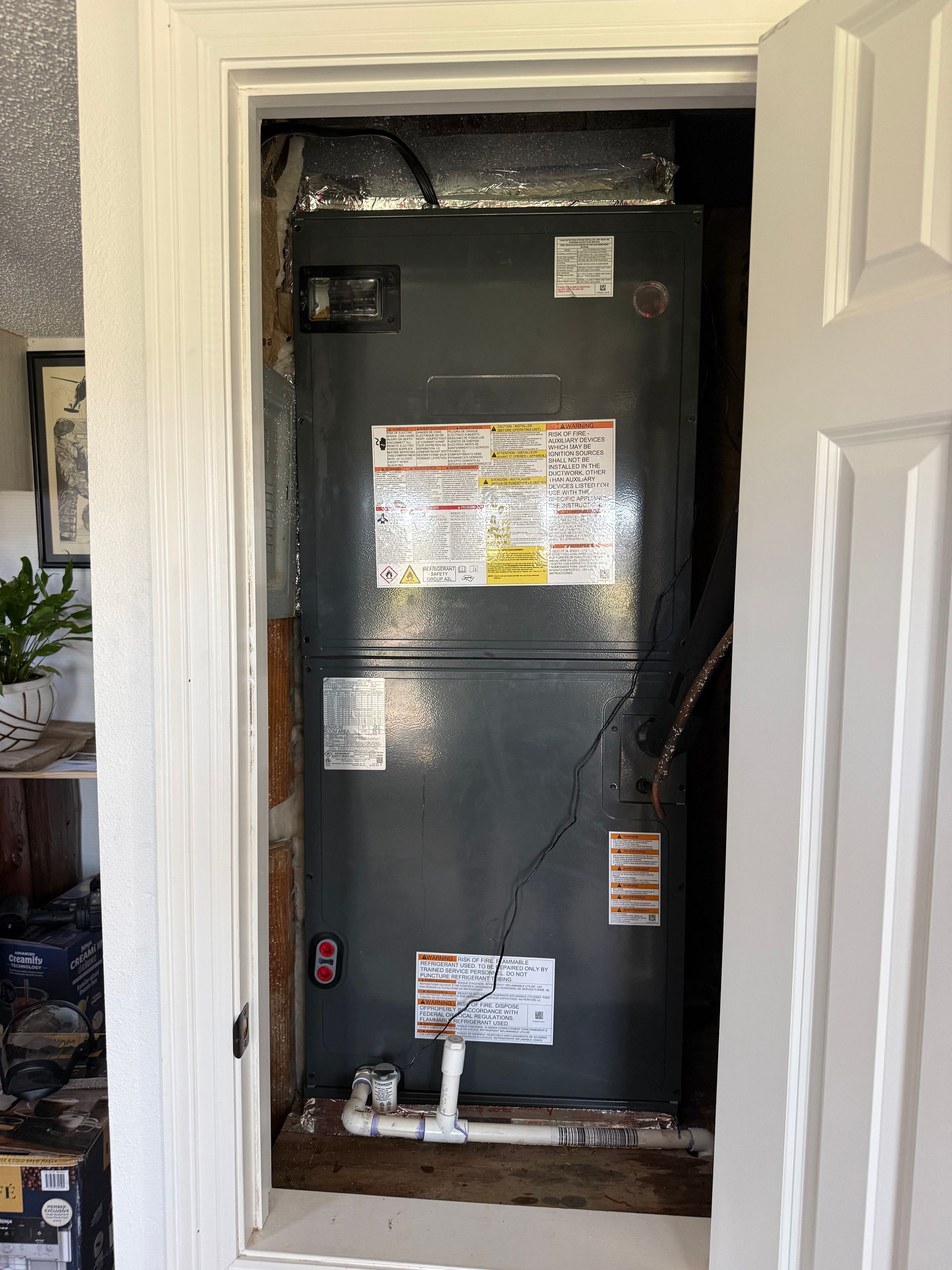 Black HVAC unit in a closet-like alcove with labels and wiring, framed by white door trim.