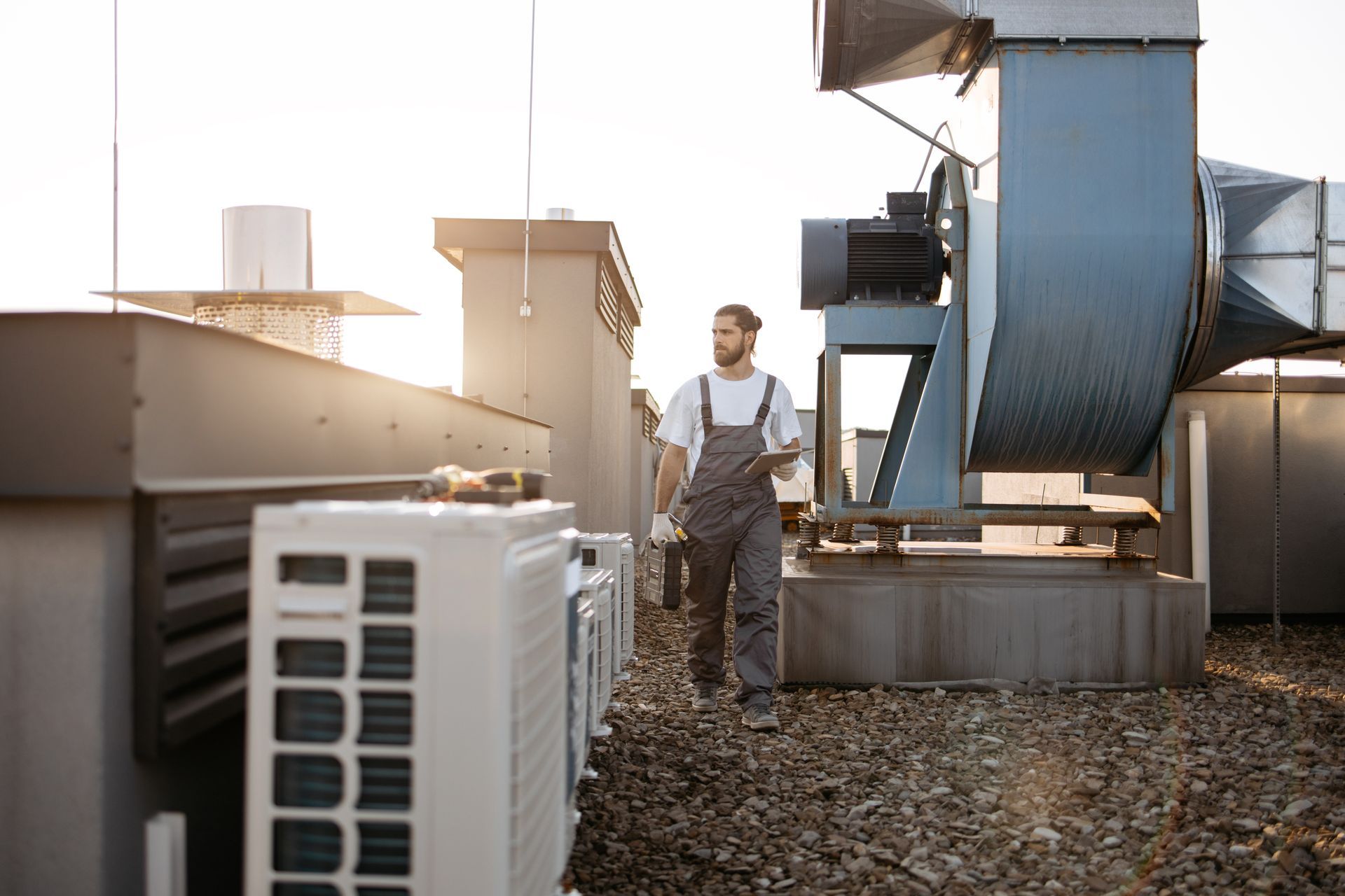 Technician standing on a rooftop beside HVAC equipment in warm sunlight