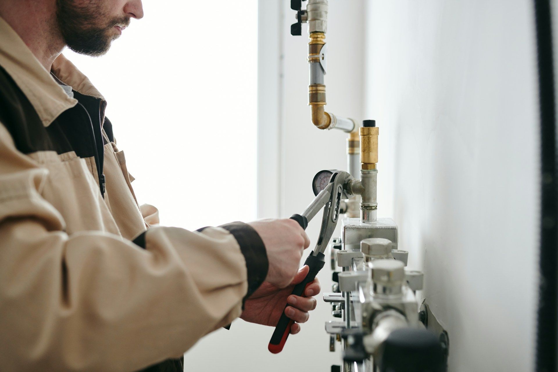 Technician tightening a pipe fitting with pliers on a wall-mounted heating system