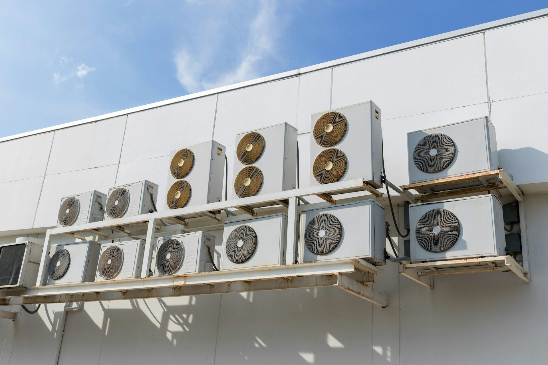 Row of outdoor air conditioning units mounted on a white building wall under a blue sky