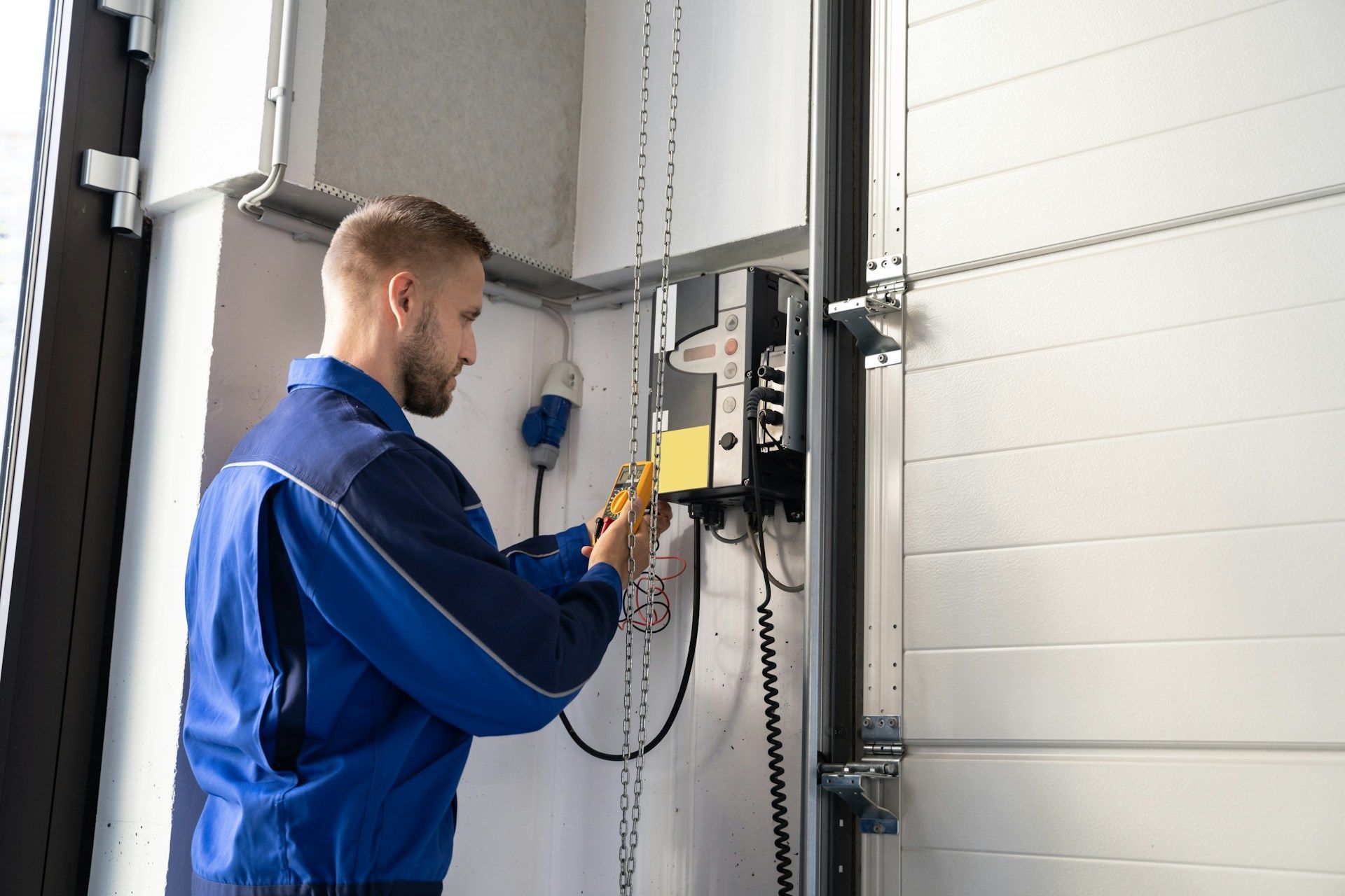 Technician in blue coveralls inspecting a control panel beside a large garage door