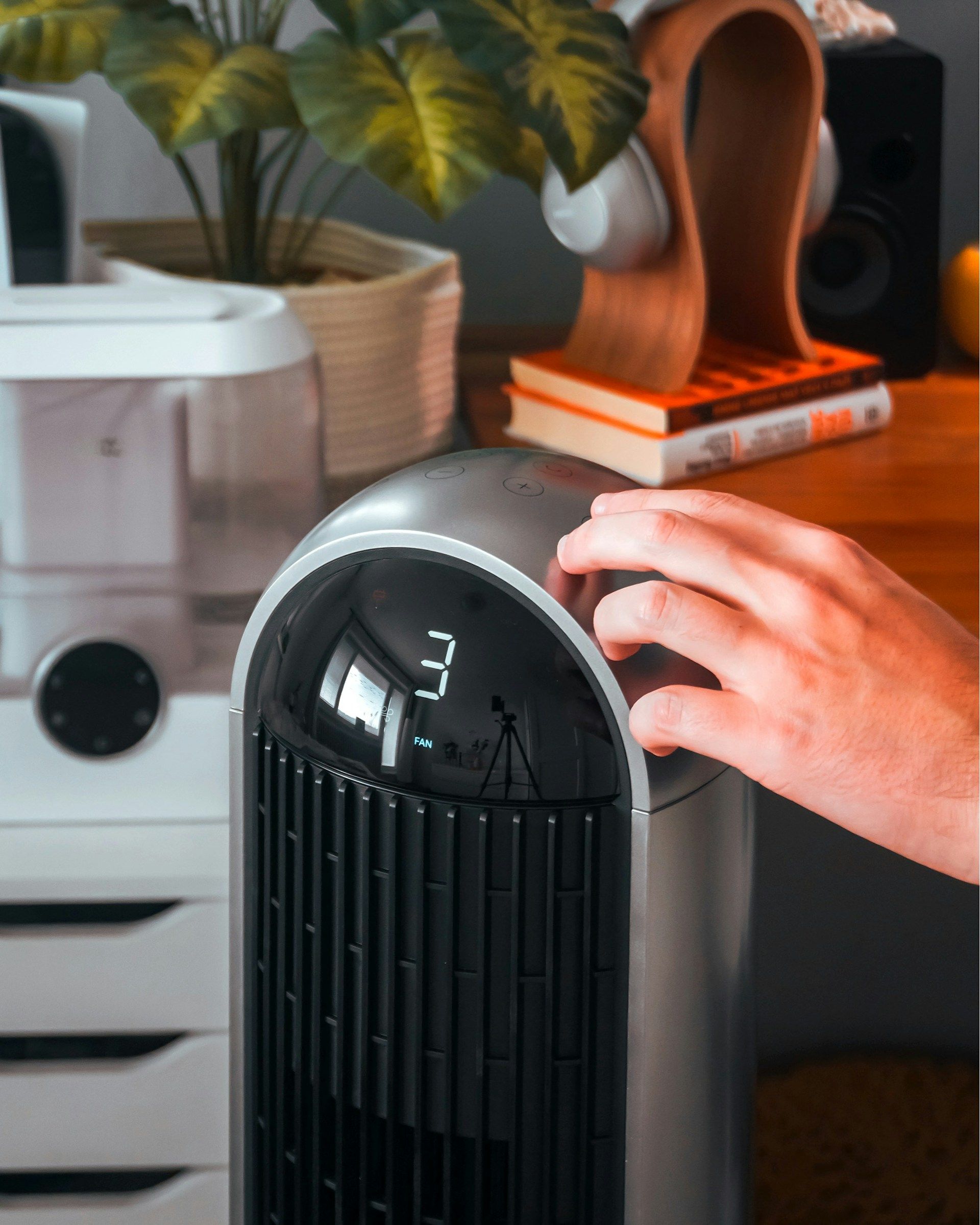 Hand on a black digital appliance in a home setting, with plants and decor in the background
