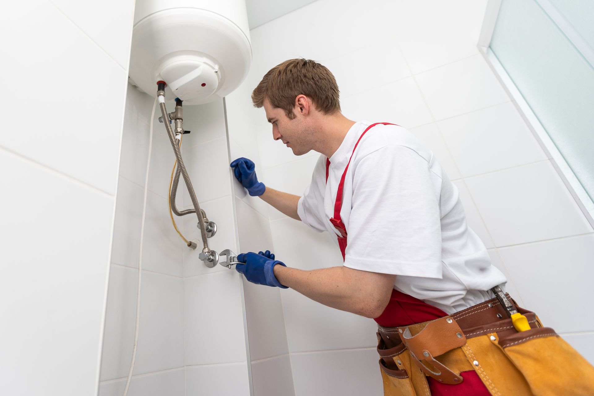 Plumber fixing pipes under a sink with tools in a tiled bathroom