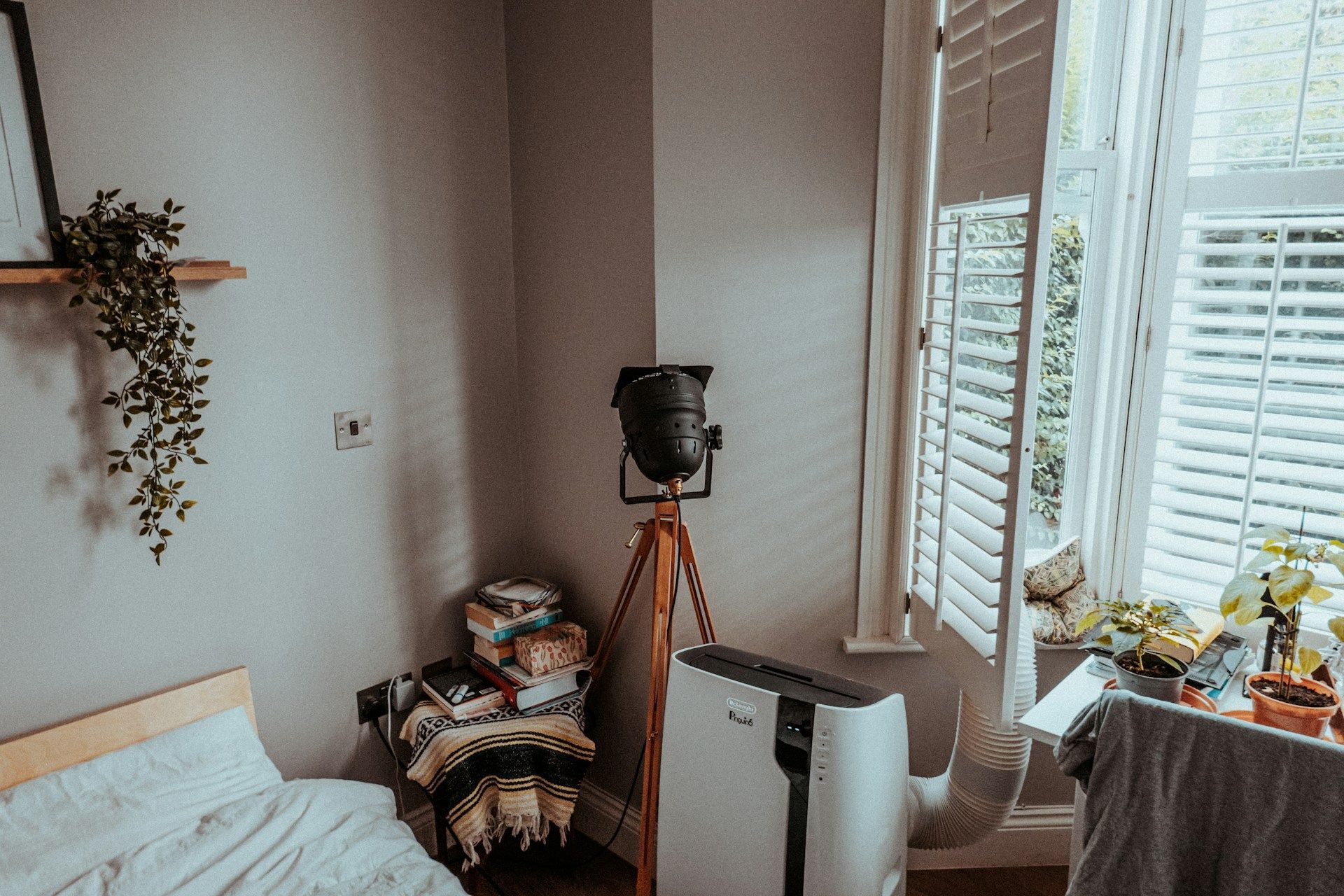 Cozy bedroom with bed, tripod-mounted camera, and sunlight through white shutters