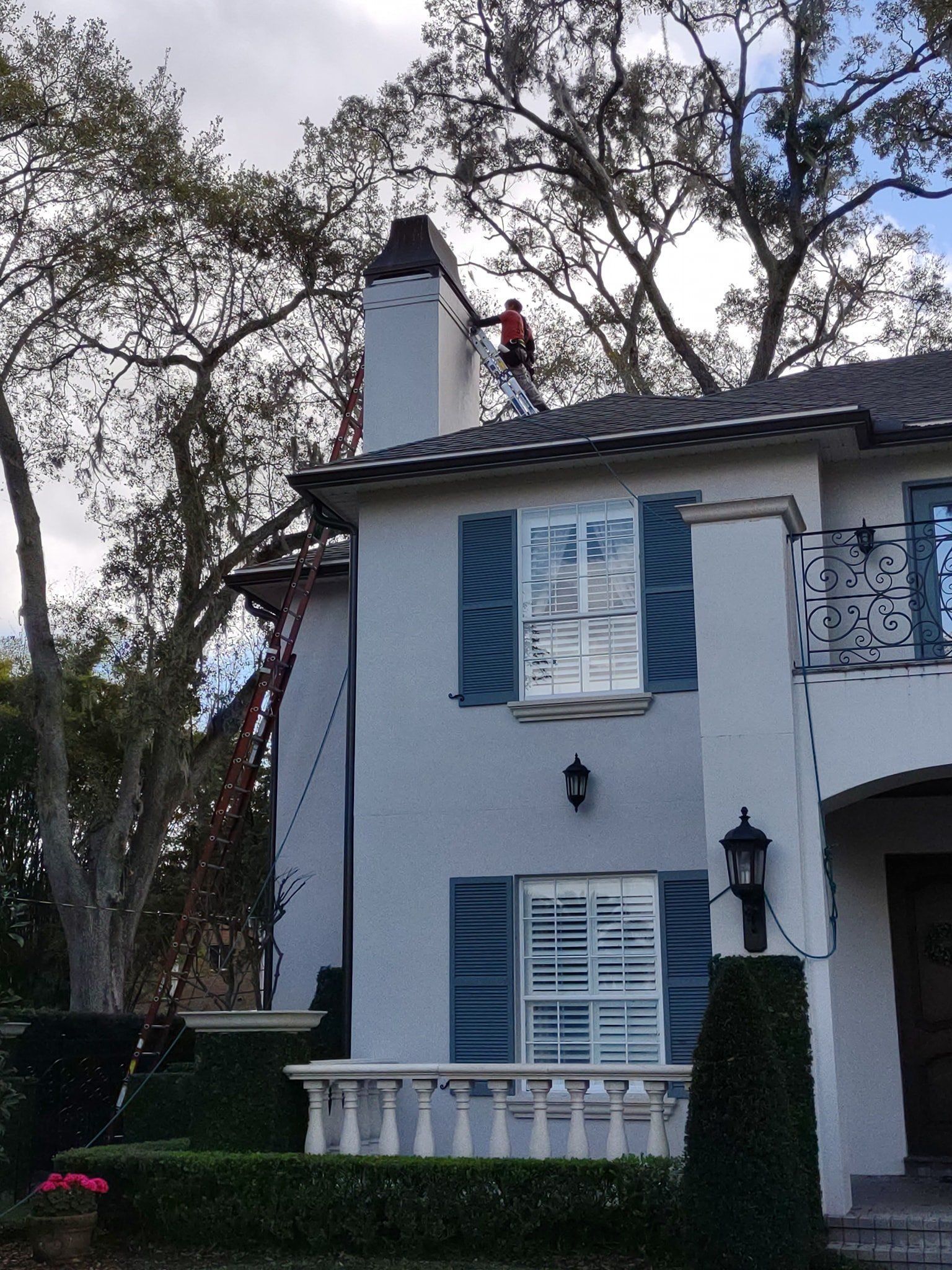 A man is painting a chimney on top of a white house