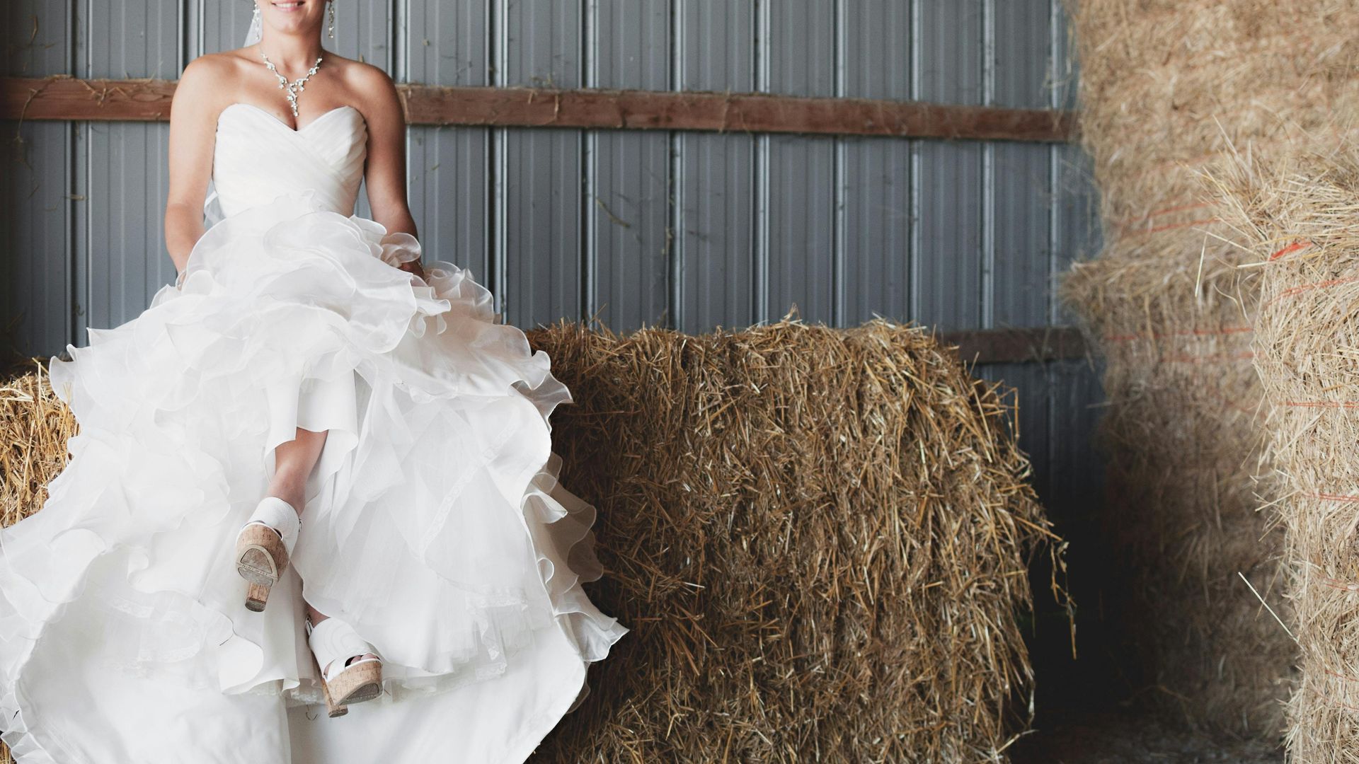 A bride in a wedding dress is sitting on a bale of hay.