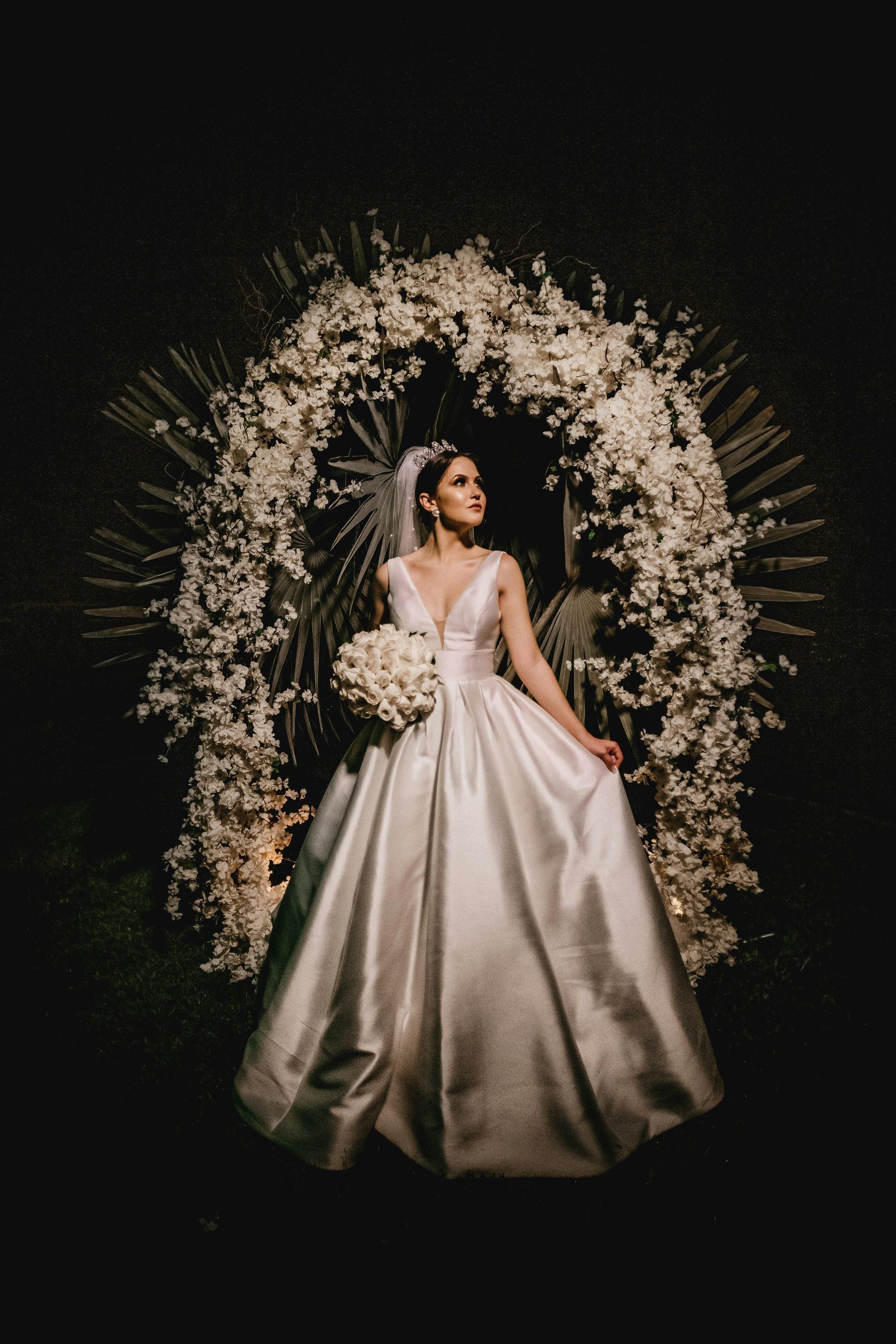 A bride in a wedding dress is standing in front of a floral arch.