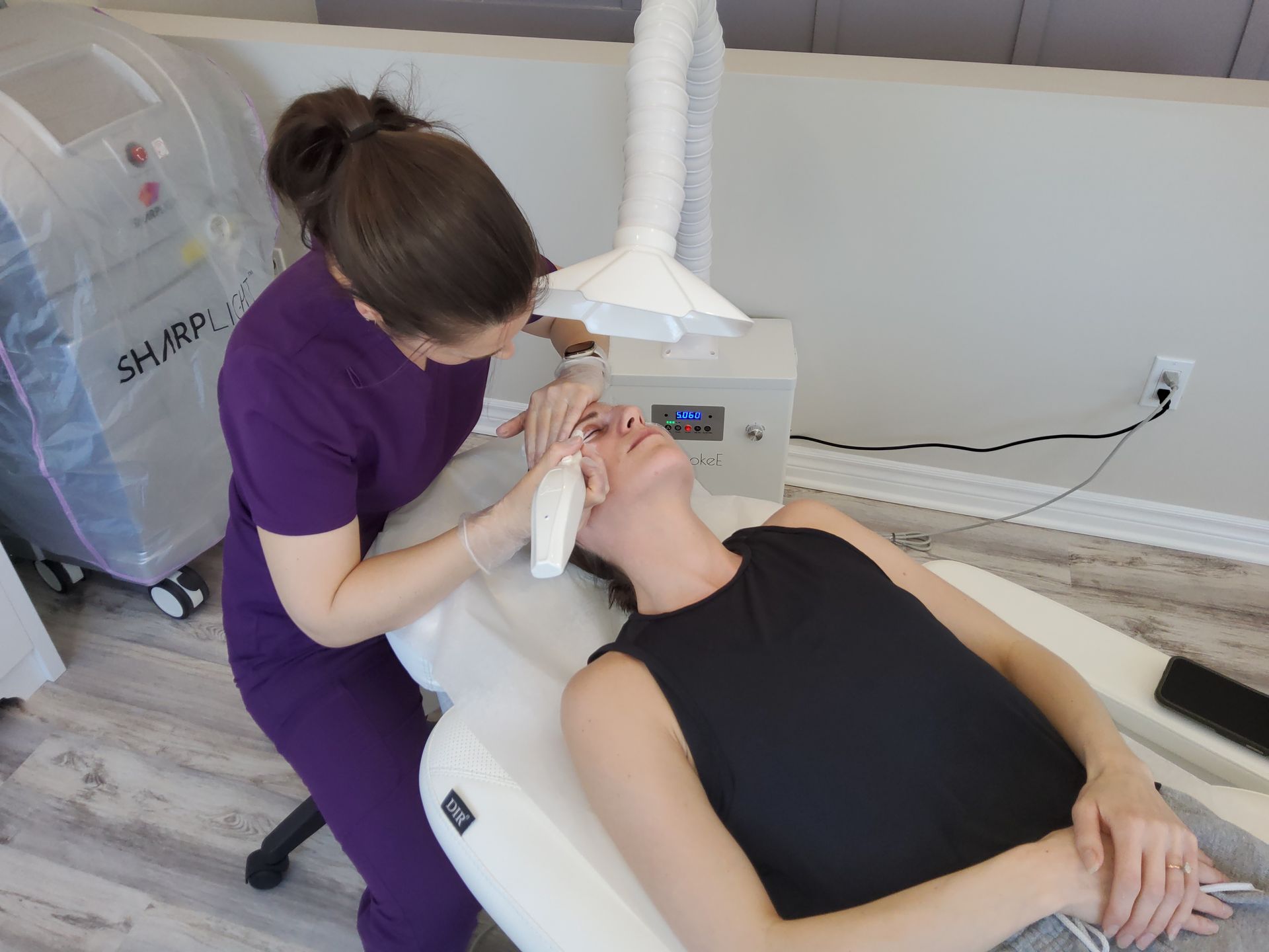 A woman in purple scrubs is cleaning a woman 's face in a chair.