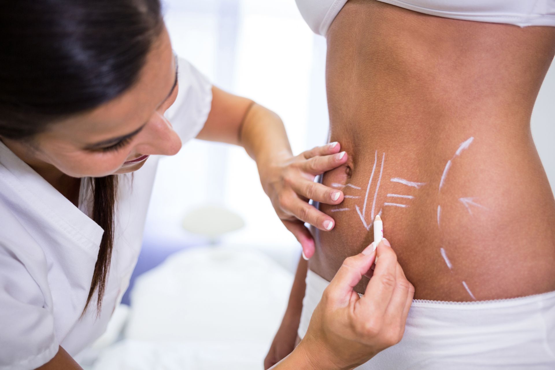 A woman is drawing lines on a woman 's stomach with a marker.