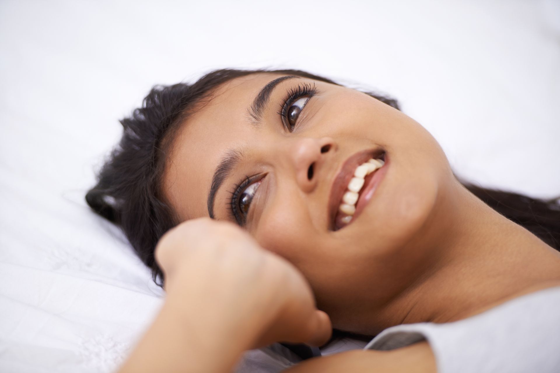 A woman is smiling while laying on a bed.