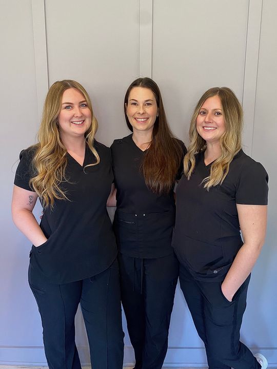 Three women in black scrubs are posing for a picture together.