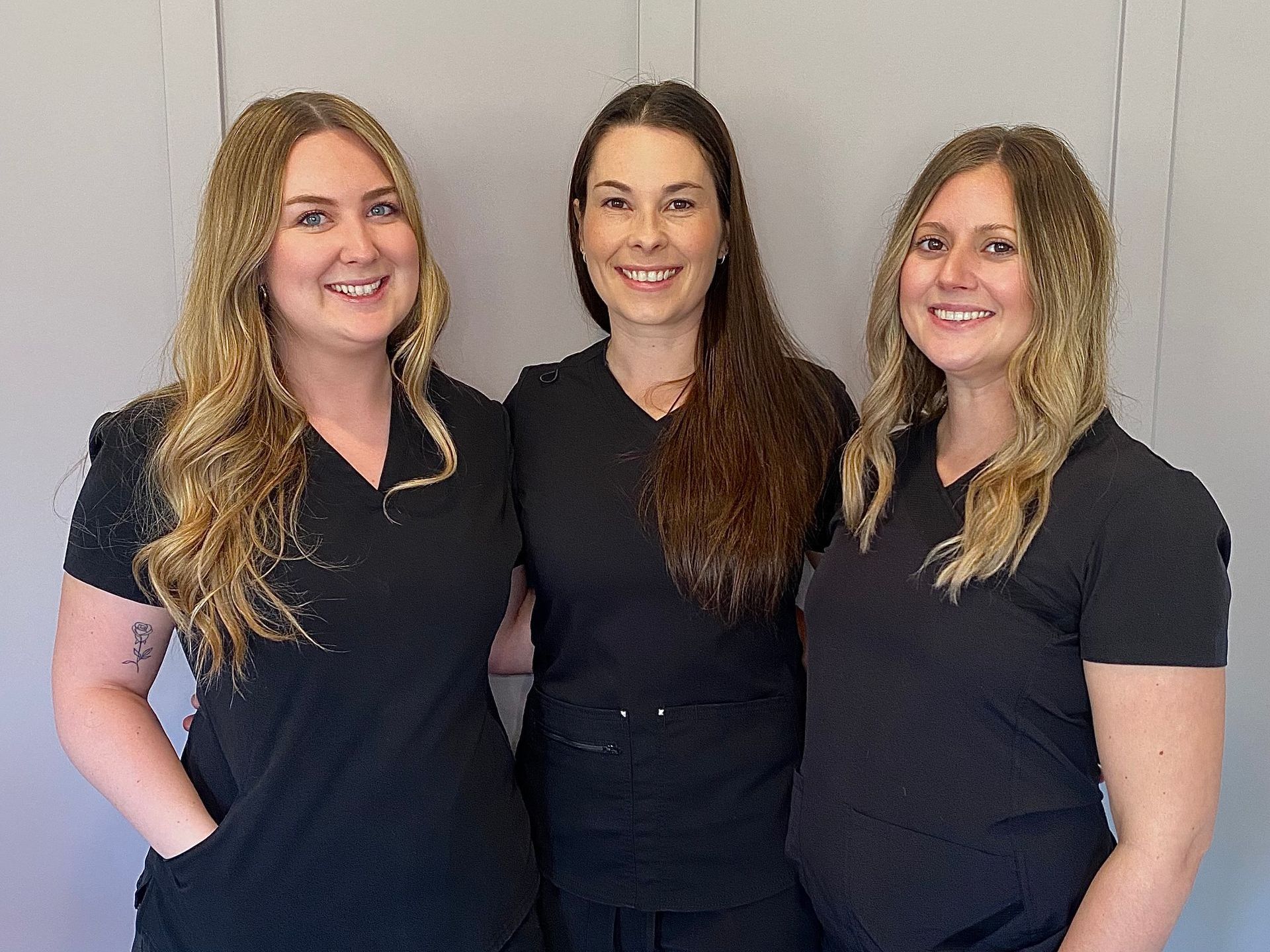 Three women in black scrubs are posing for a picture.