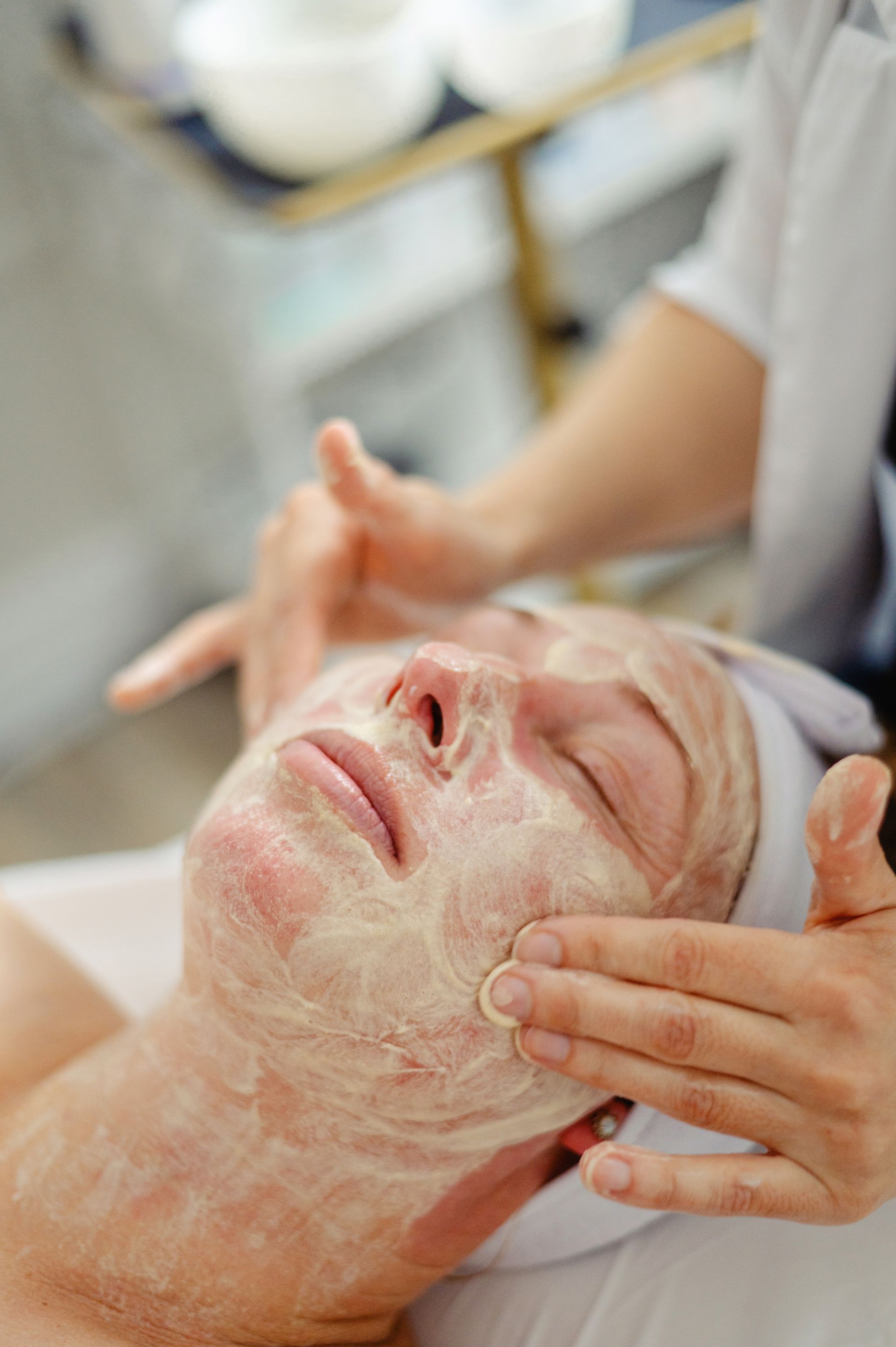 A woman is smiling while applying cream to her face.