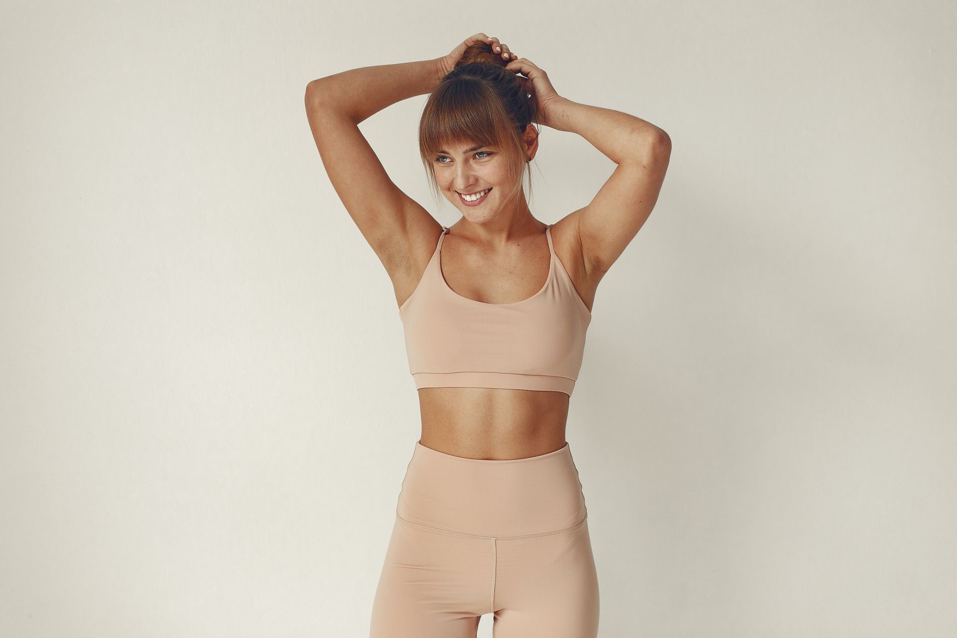 A woman in a sports bra and shorts is standing in front of a white wall.