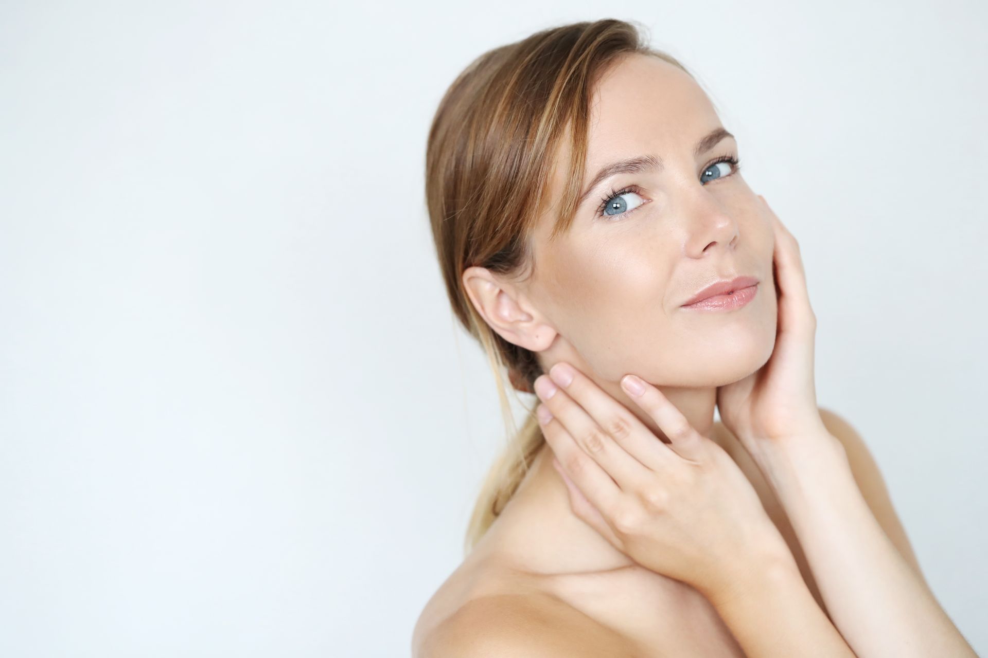 A woman is touching her face with her hands and smiling.