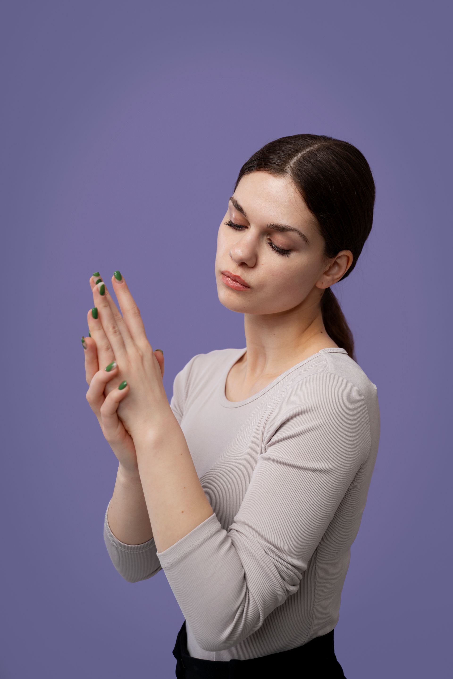 A woman with green nails is holding her hands together on a purple background.