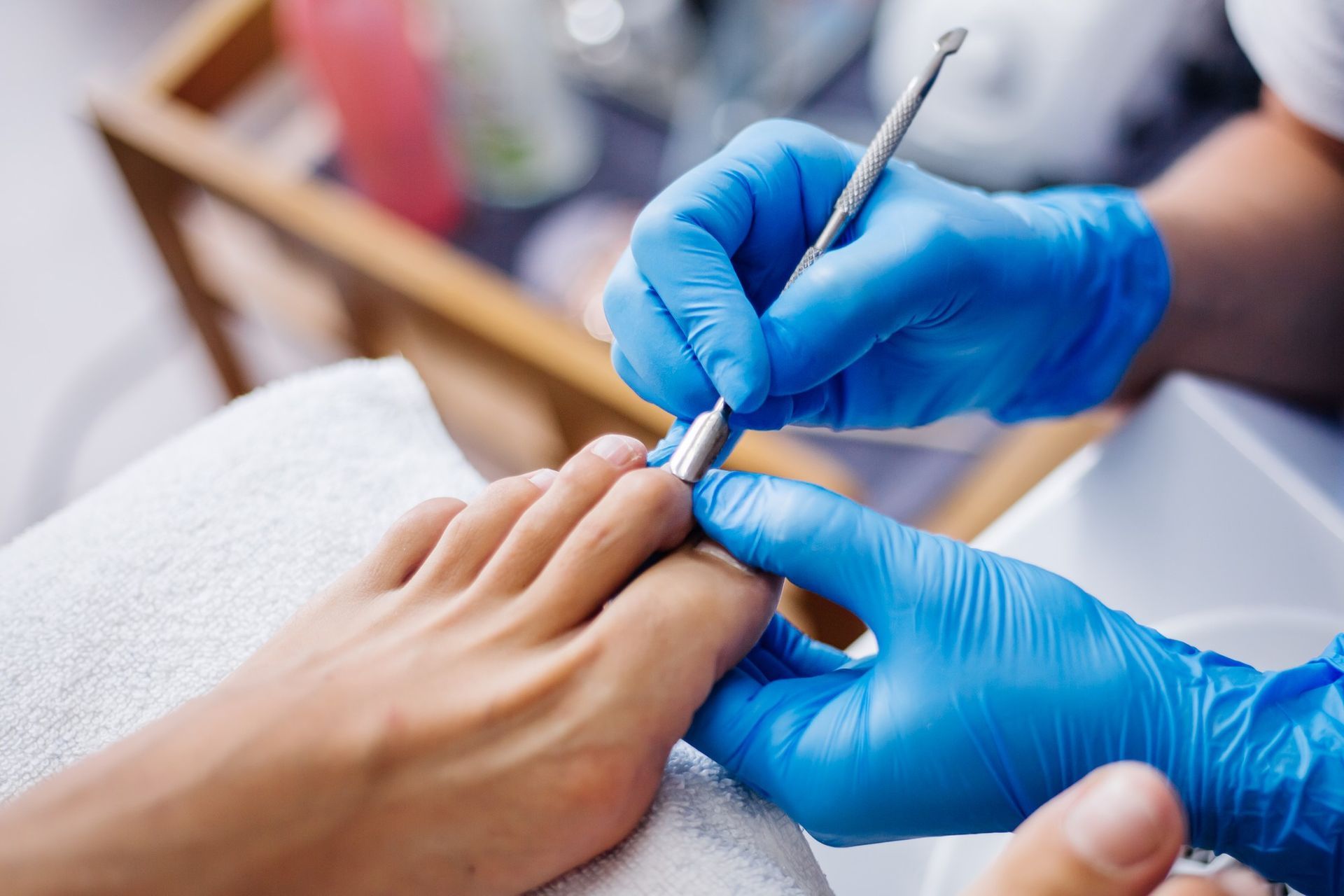 A woman is getting her toenails done by a nail technician wearing blue gloves.