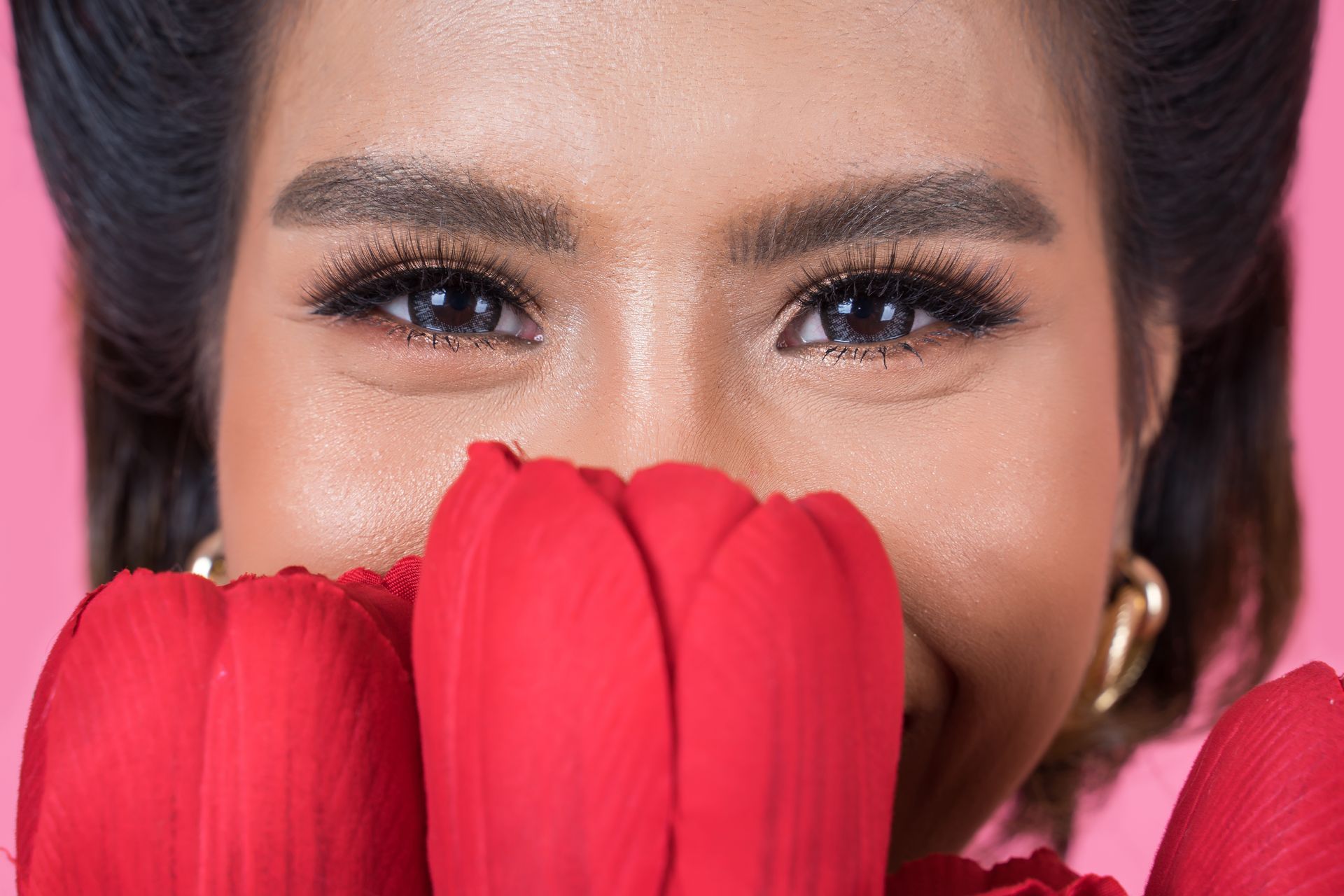 A woman is covering her face with a red flower.