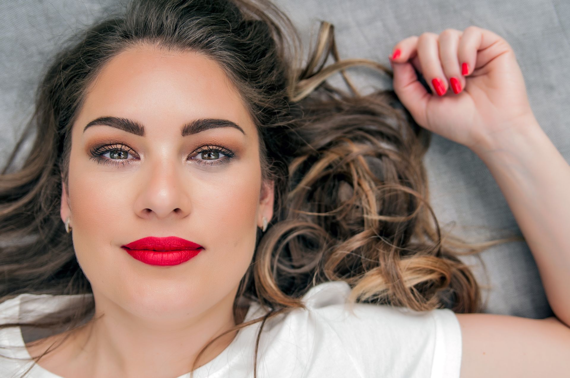 A woman with red lipstick and red nails is laying on the floor.