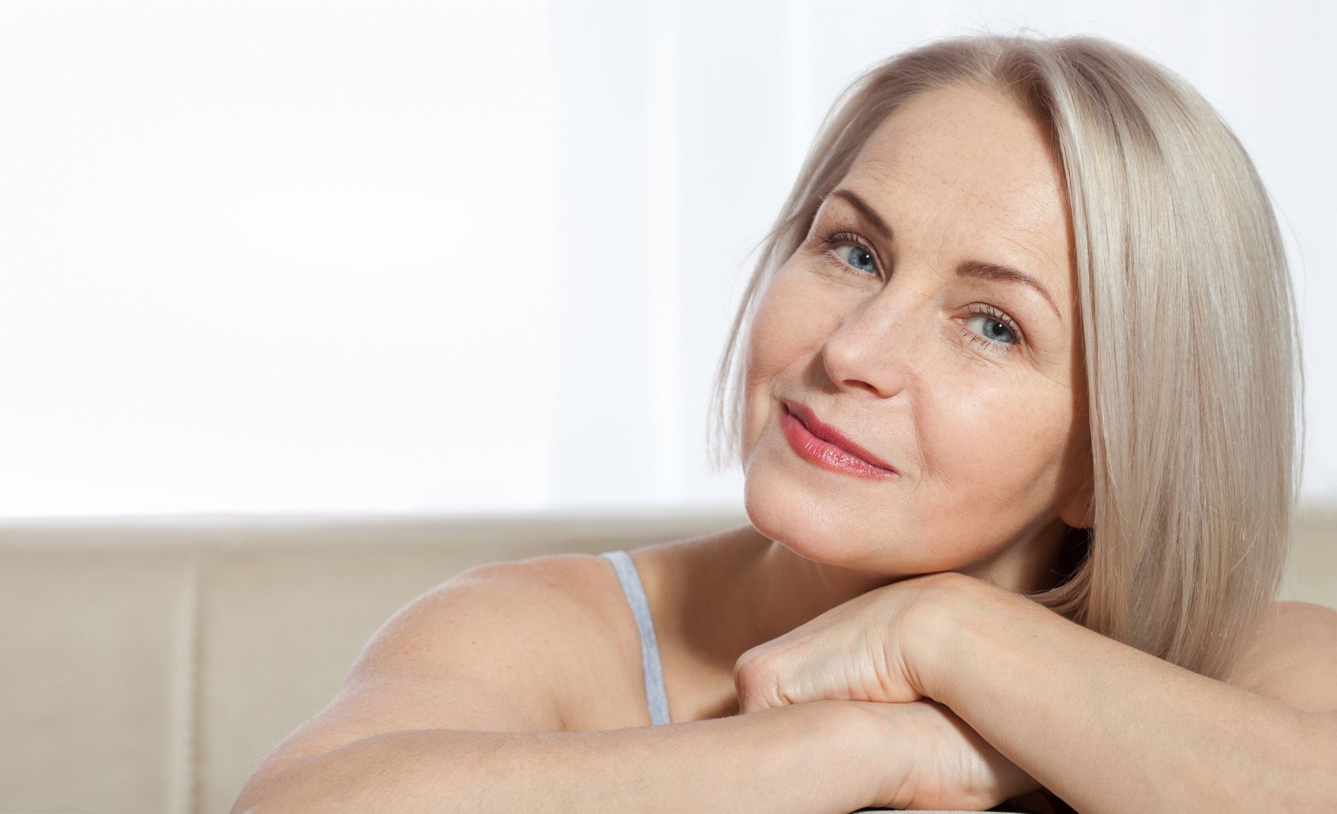 A woman is sitting on a couch with her hands on her face.