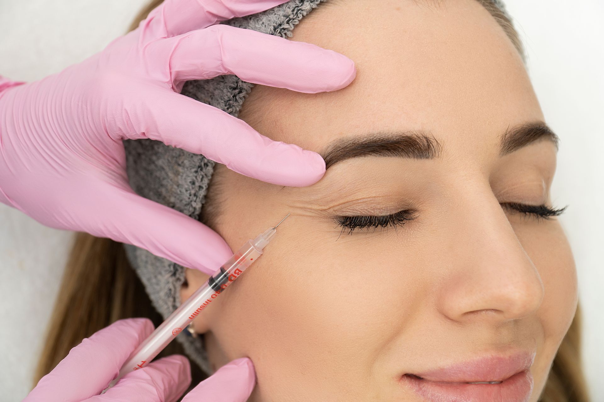 A woman is getting a botox injection in her forehead.