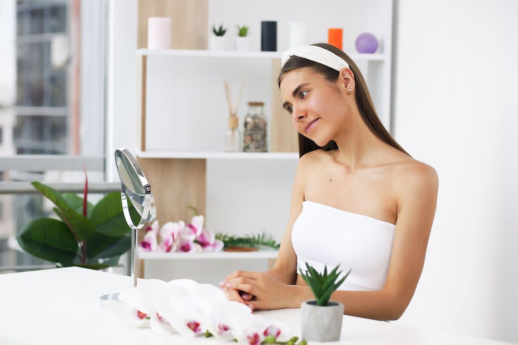 A woman is sitting at a table looking at her face in a mirror.