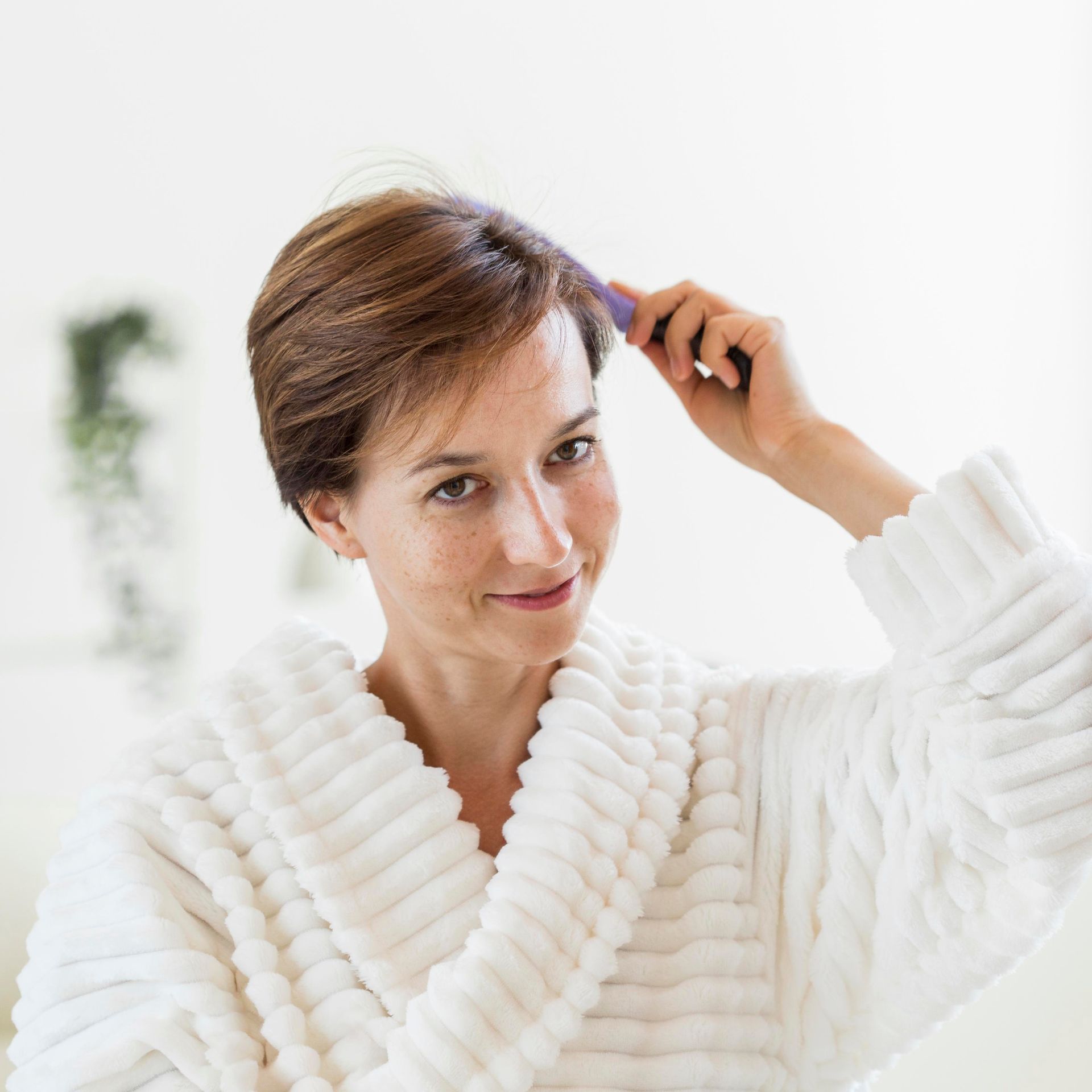 A woman in a white robe is brushing her hair