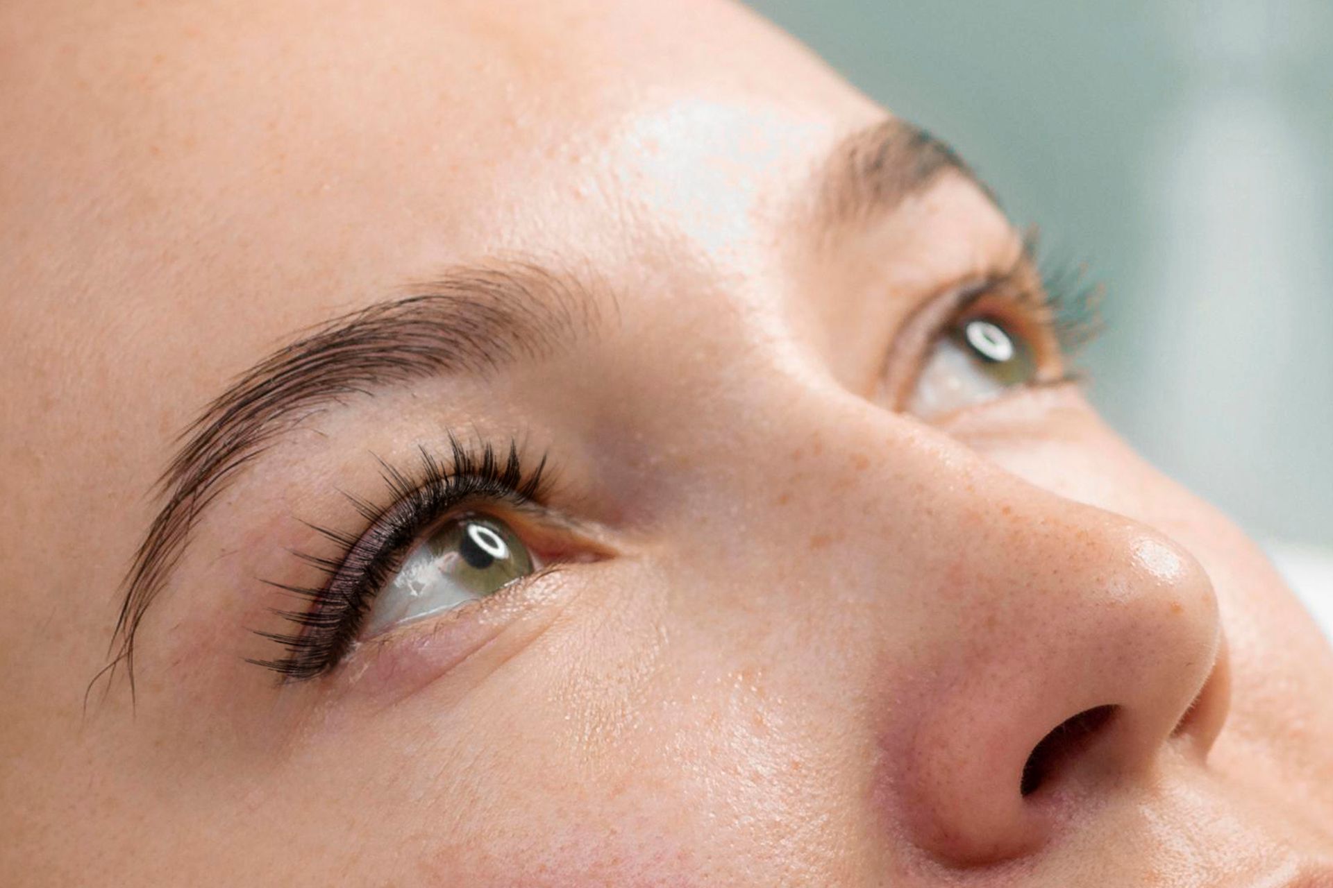 A close up of a woman 's face with green eyes and long eyelashes.