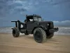 Black military tow truck on a sandy beach under a cloudy sky.