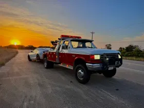 Tow truck towing a car on a road at sunset. The truck is red and white.