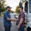 Two men shaking hands beside a tow truck on a residential street at sunset.