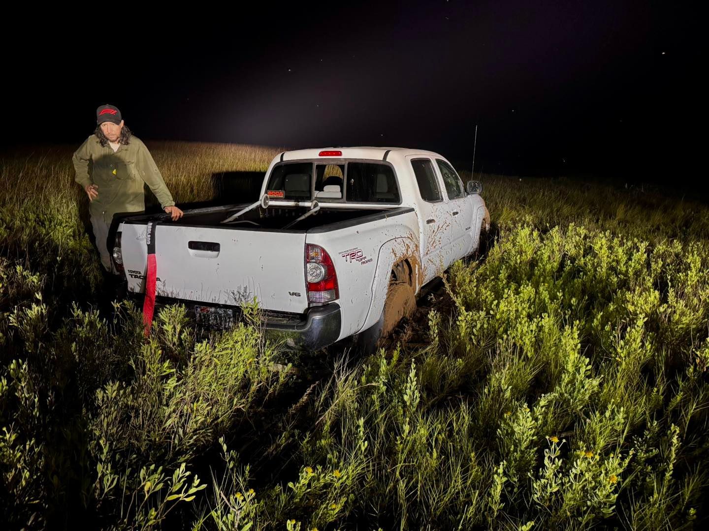 White truck stuck in tall grass at night; person stands beside it.