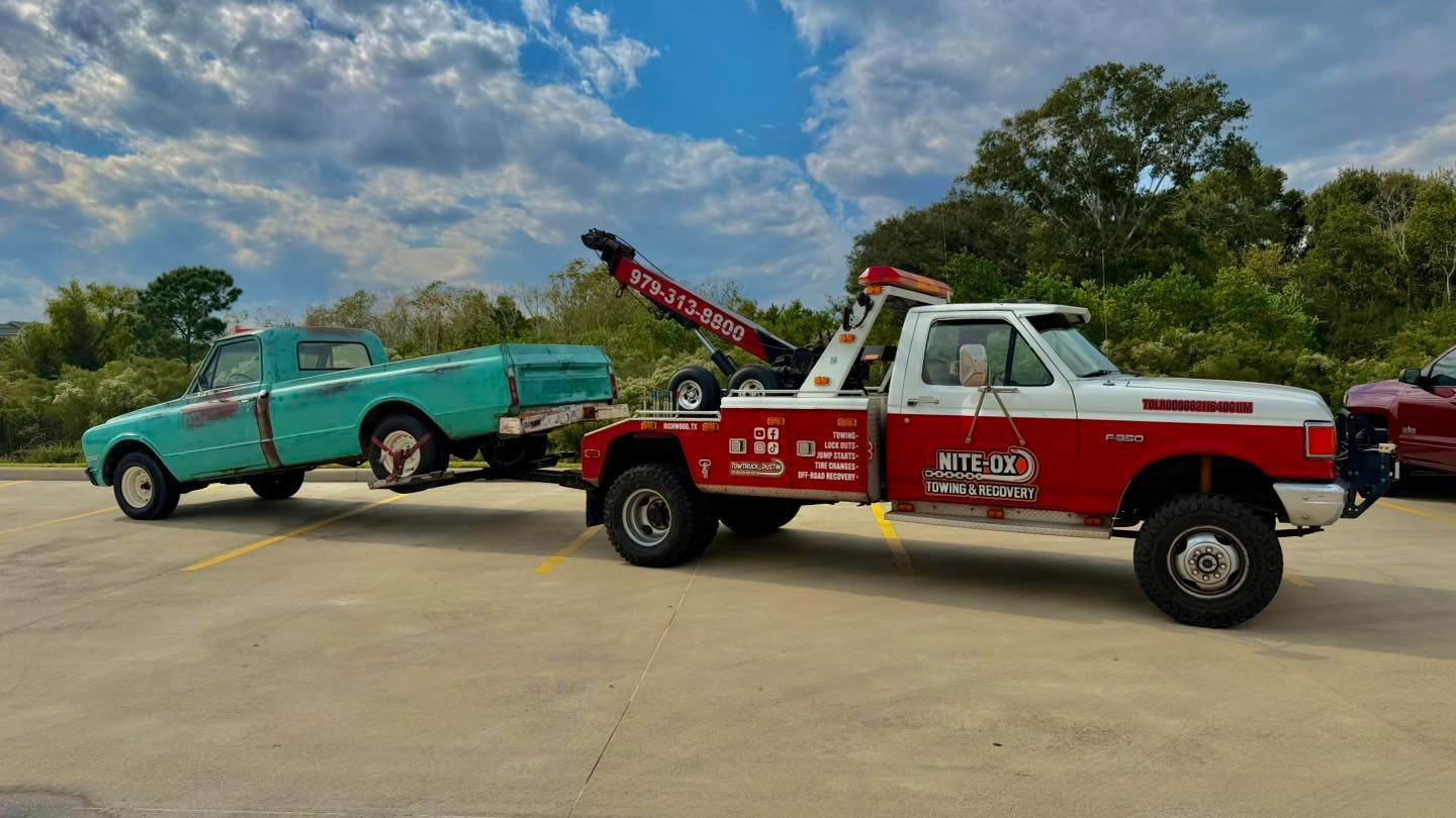 Tow truck towing a light blue pickup truck on a bright day. Red and white tow truck has a red boom.