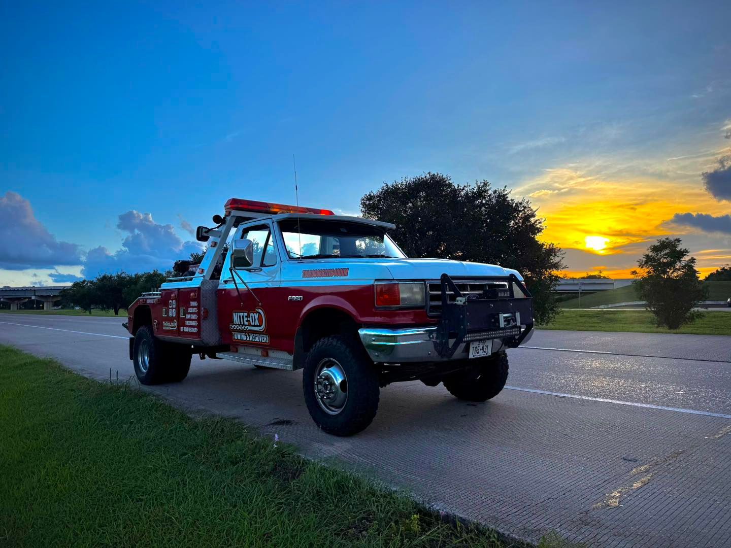 Red and white tow truck parked on road with sunset in background.