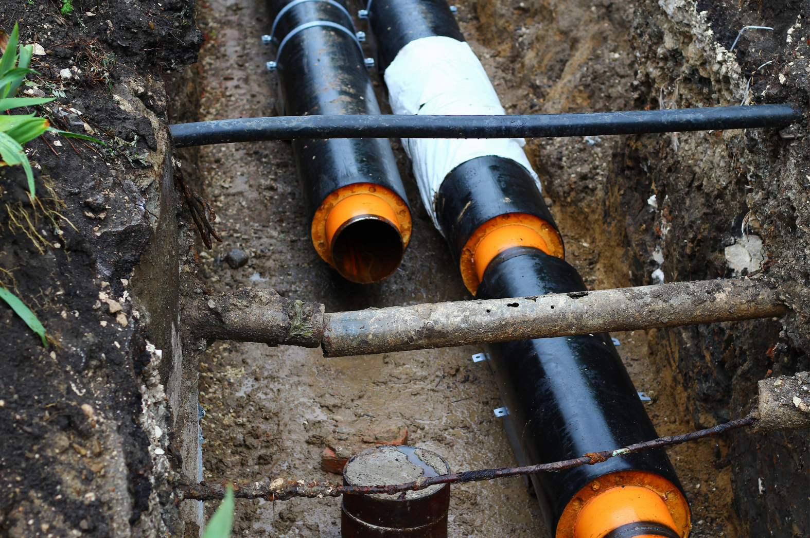 Two large black pipes with orange ends laid in an excavated trench, surrounded by moist soil. 