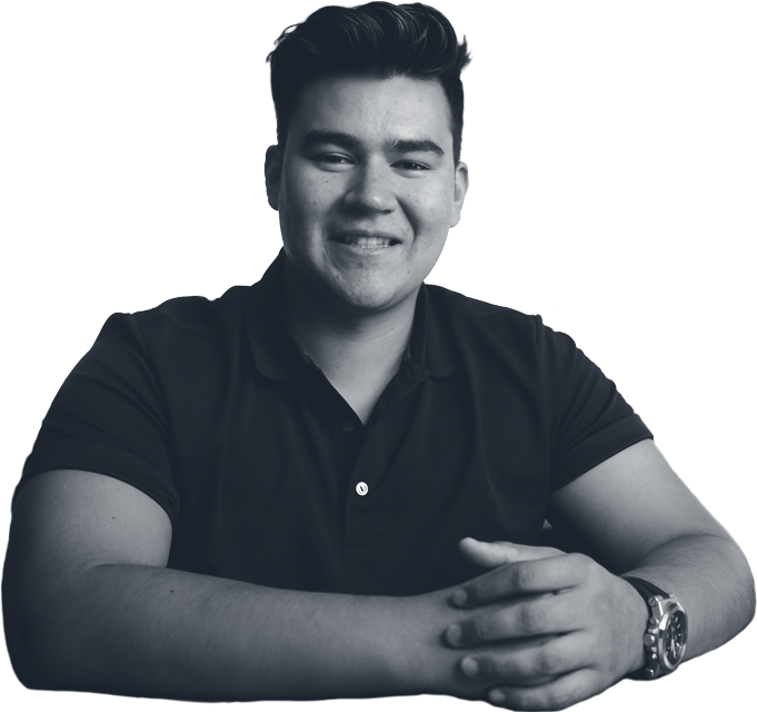 A smiling person with dark hair and a watch, resting arms on a surface.