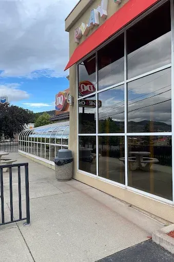 Dairy Queen exterior with red awning, large windows, and outdoor seating area. Blue sky in background.