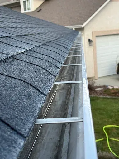 Gutter filled with debris next to a dark gray shingled roof on a beige house.