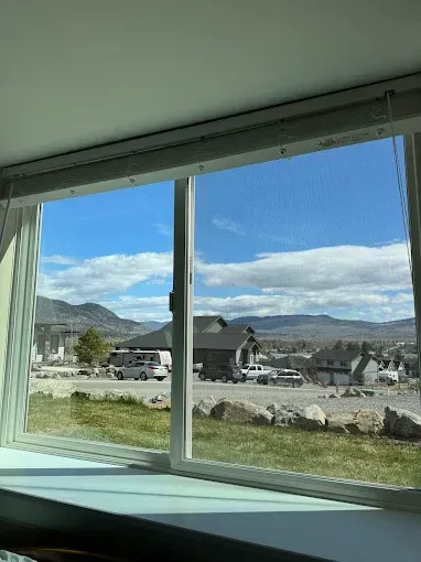 View through a window of a suburban landscape: houses, mountains, blue sky with clouds.