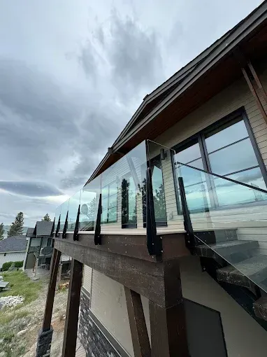 Glass railing on a deck of a house, set under a cloudy sky.